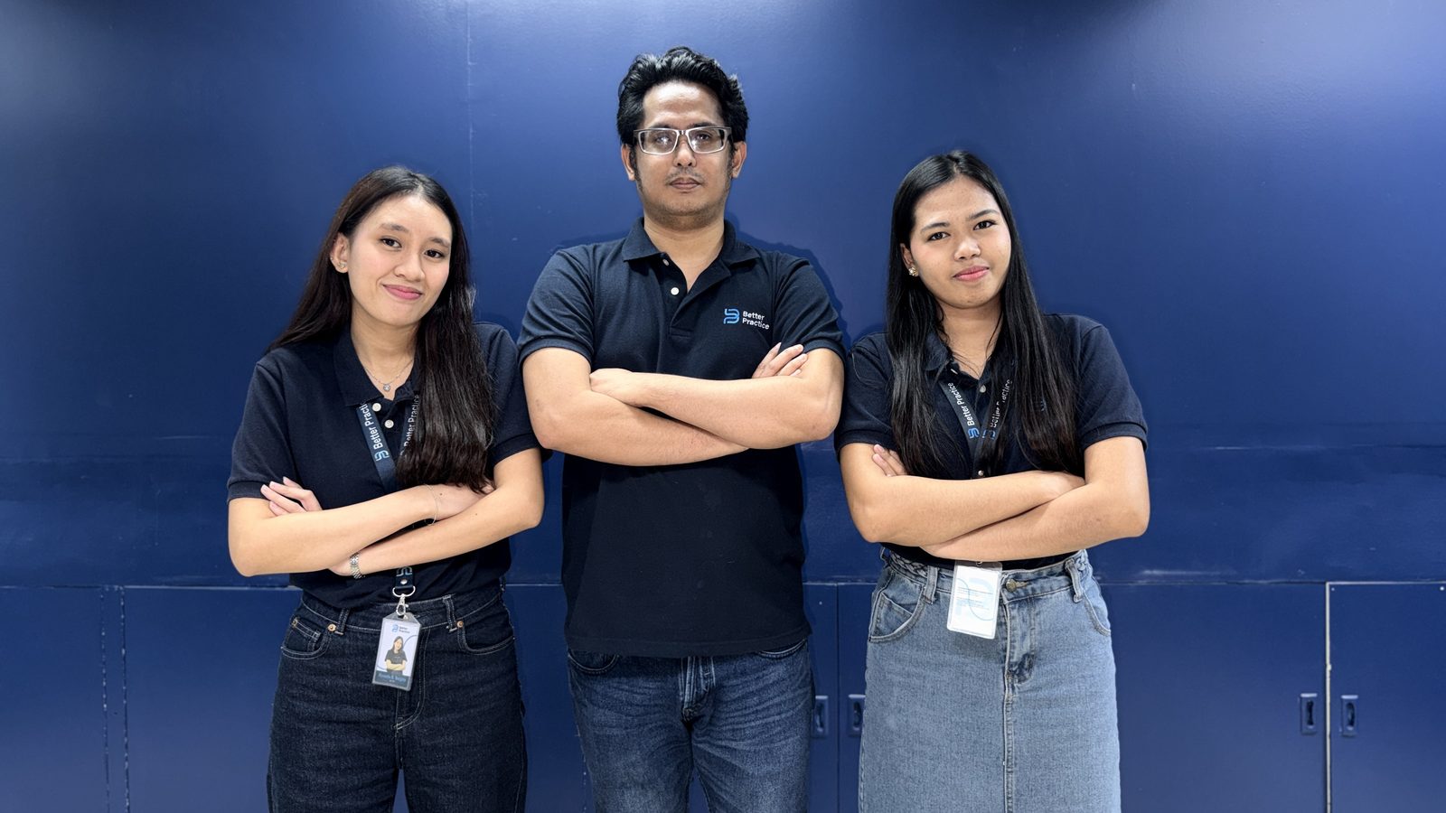 The technology team standing with arms folded against the navy office wall